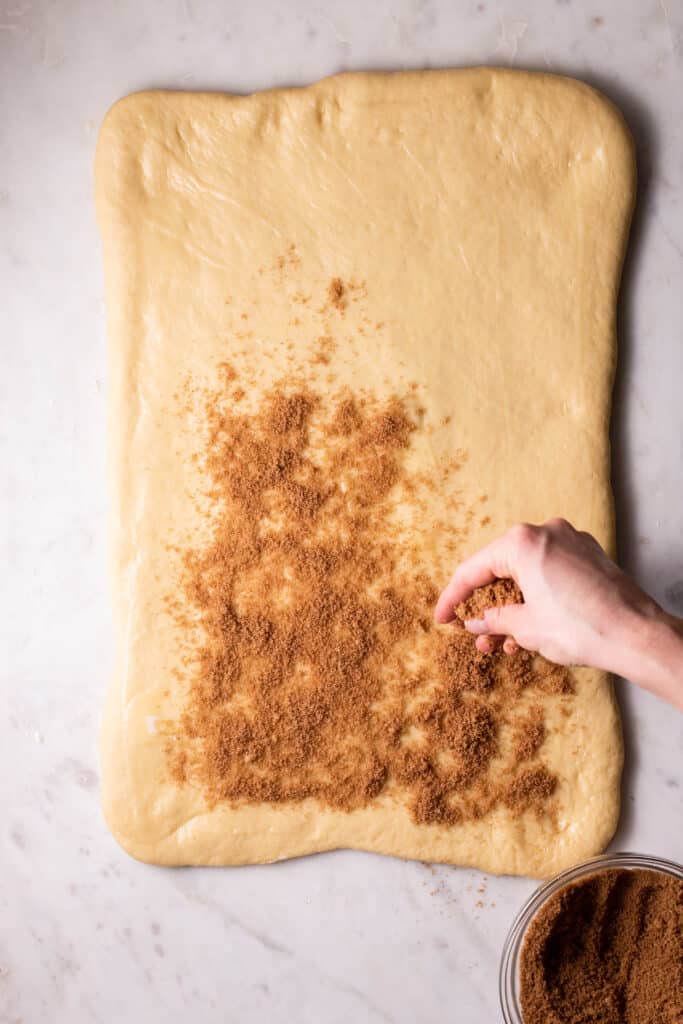 hand sprinkling filling onto cinnamon roll dough