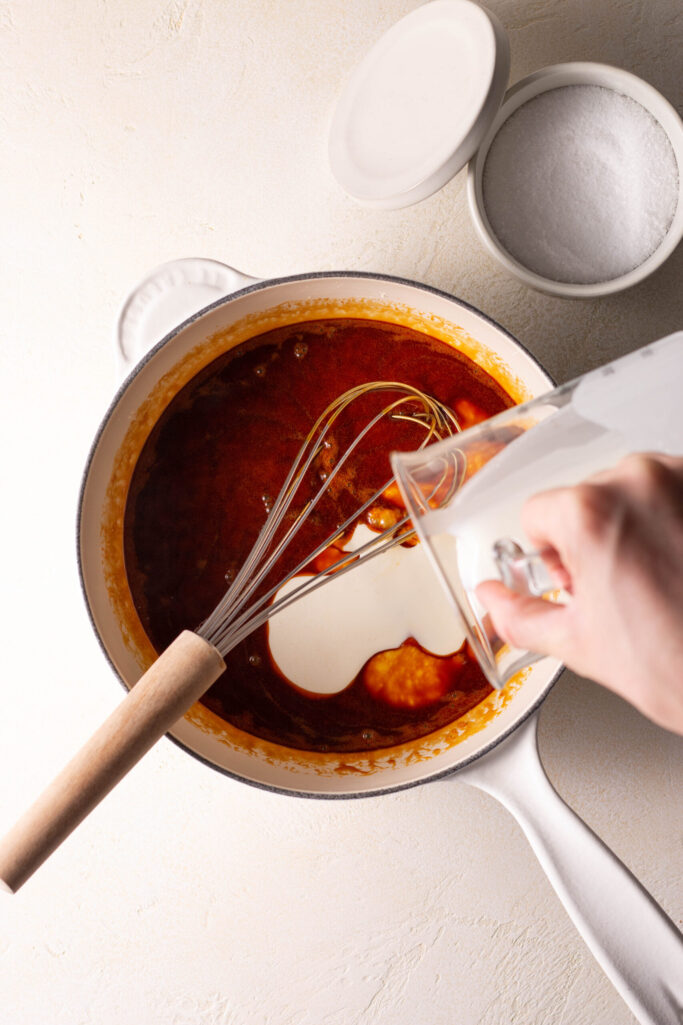 hand stirring heavy cream into a saucepan with caramel sauce