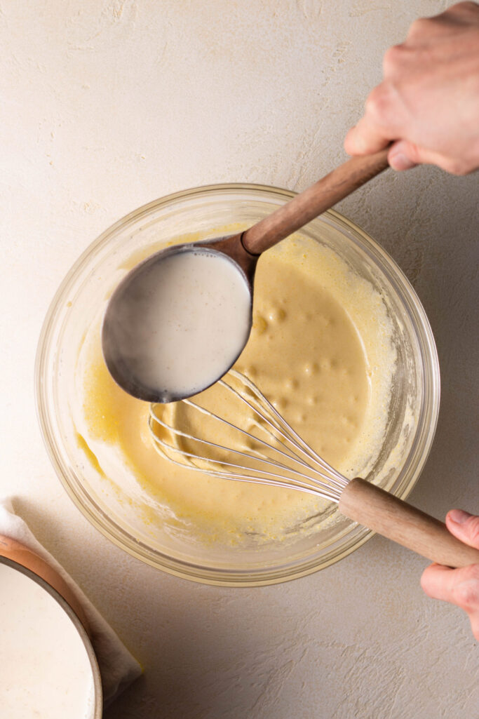 hand whisking custard in a bowl while adding warm cream.