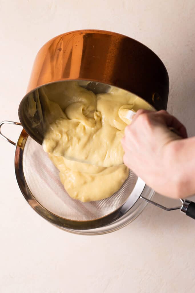 pouring pastry cream through a fine mesh sieve