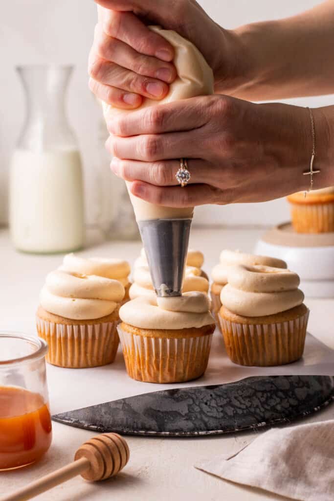 hands piping salted caramel buttercream onto brown sugar cupcakes.