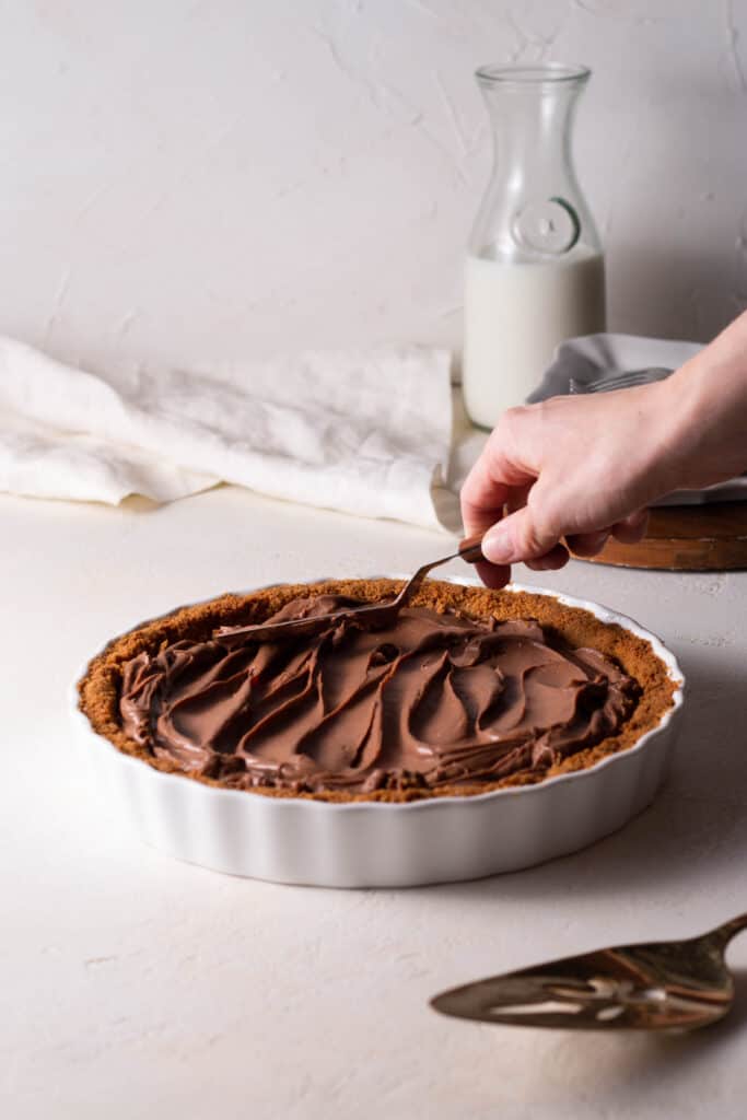 hand smoothing out chocolate pastry cream on a graham cracker crust