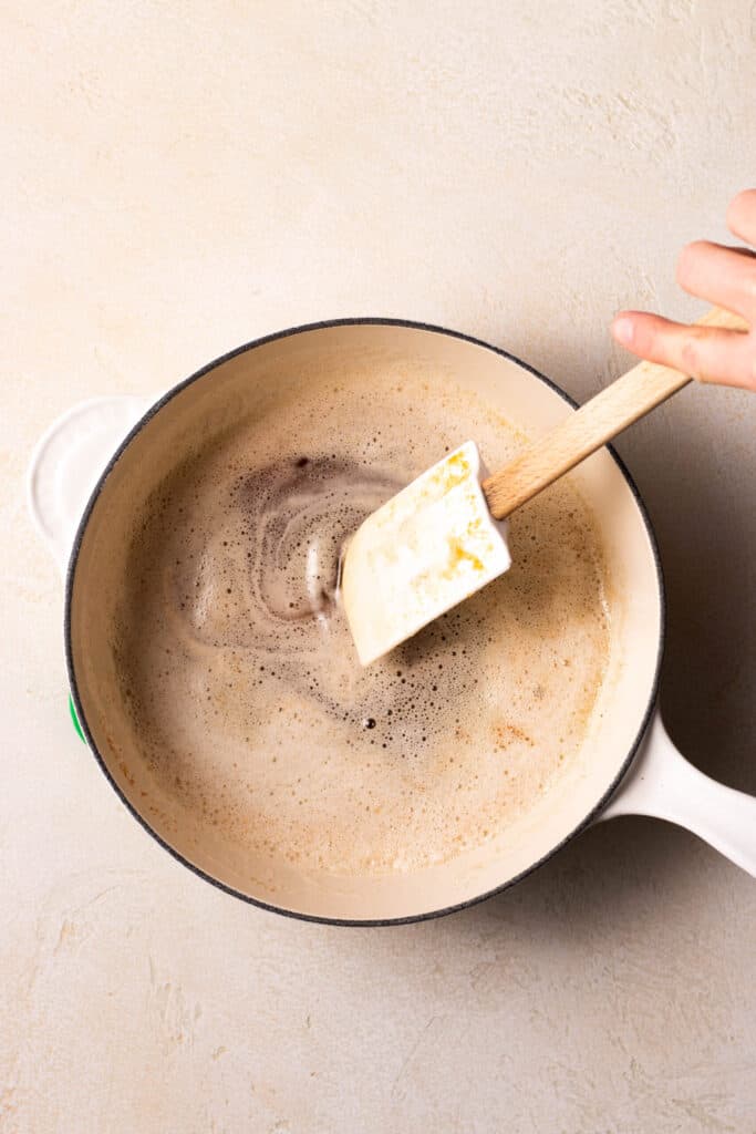 hand stirring brown butter in a saucepan.