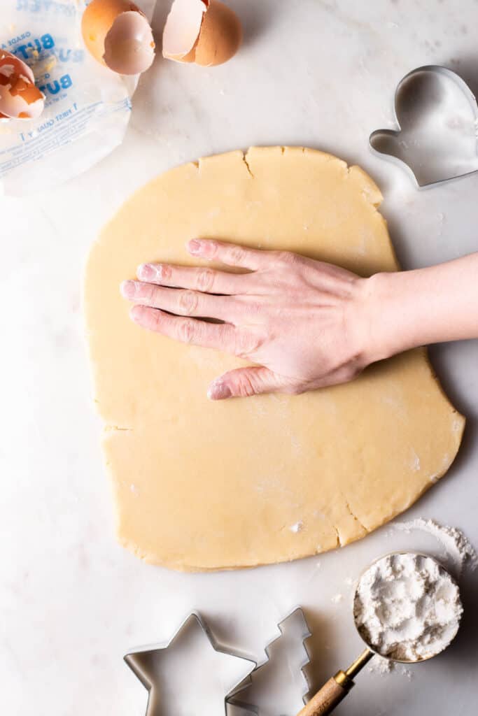 hand smoothing out cookie dough on a floured surface.