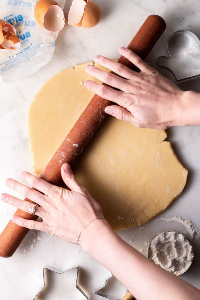 2 hands rolling out cookie dough on a floured surface