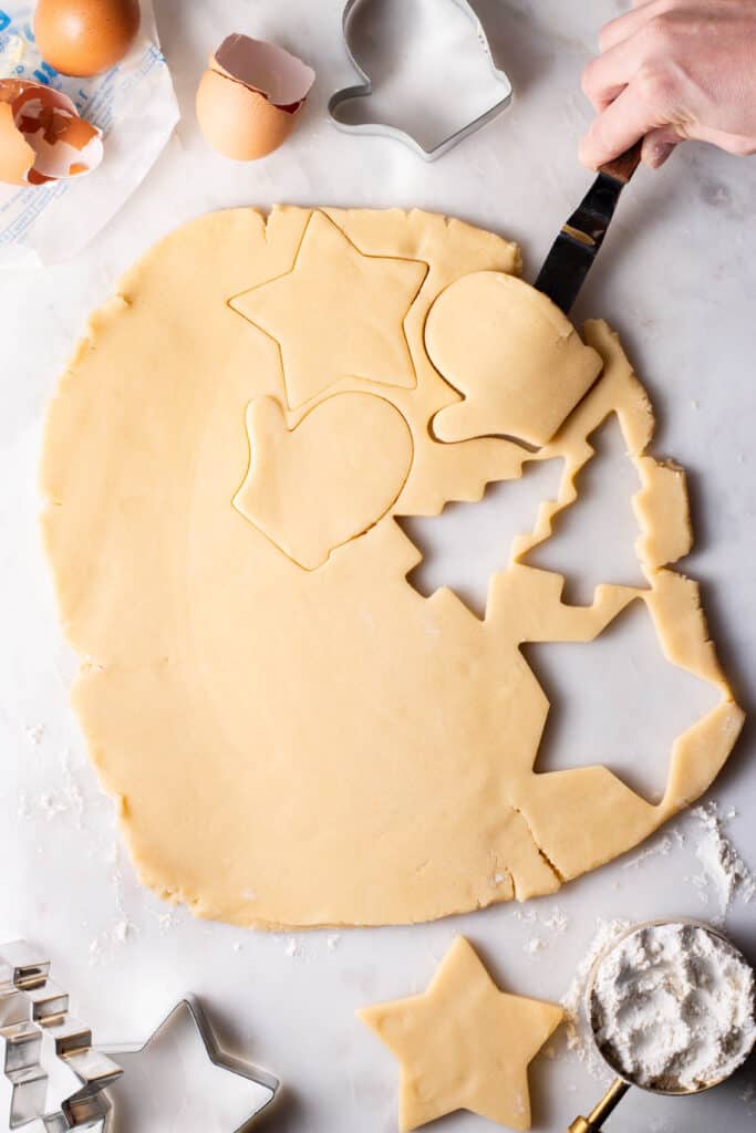 offset spatula lifting sugar cookie cut-outs from floured surface to a baking sheet