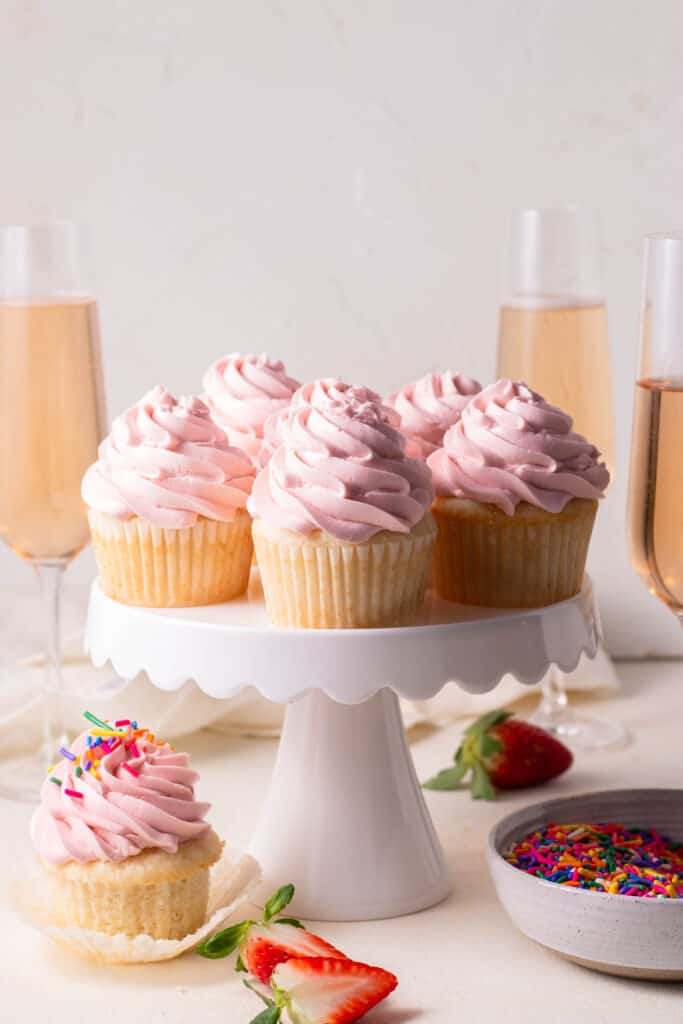 champagne cupcakes on a cake stand with sparkling wine in the background