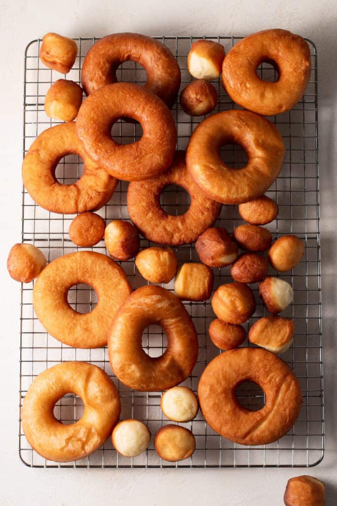 fresh yeasted donuts that are un-glazed on a cooling rack.