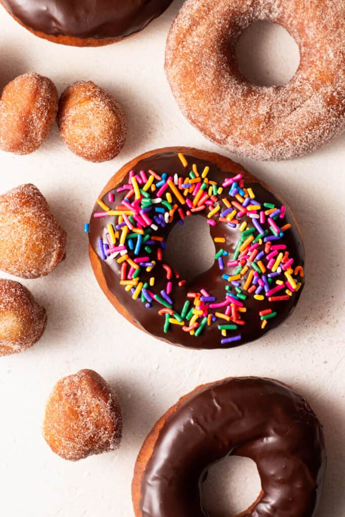 chocolate glazed donut with sprinkles surrounded by homemade donut holes on a board.