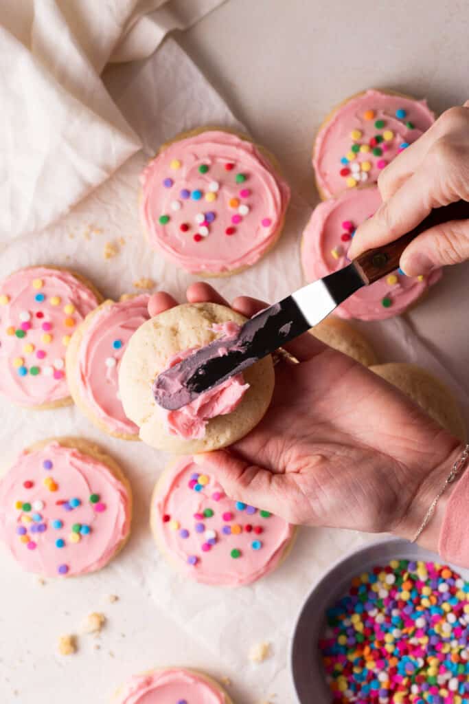 hand spreading frosting on soft sugar cookie