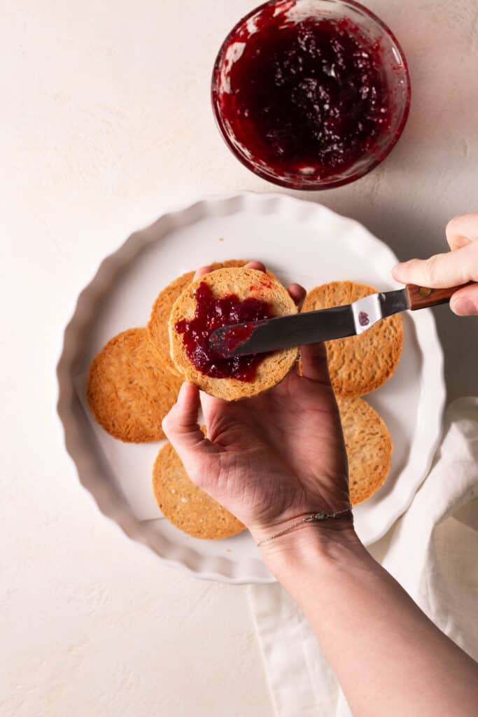 hand spreading jam on a linzer cookie