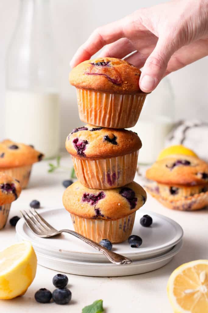 hand holding a blueberry muffin stacked on top of other muffins