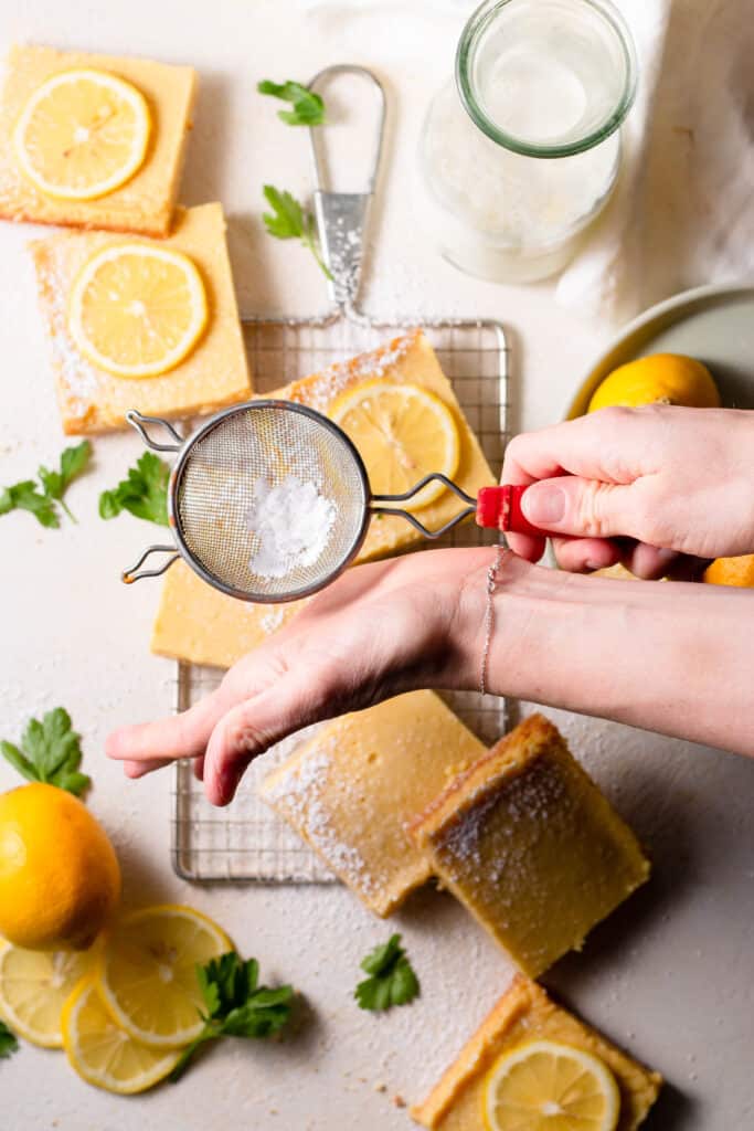 hand dusting powdered sugar on lemon bars