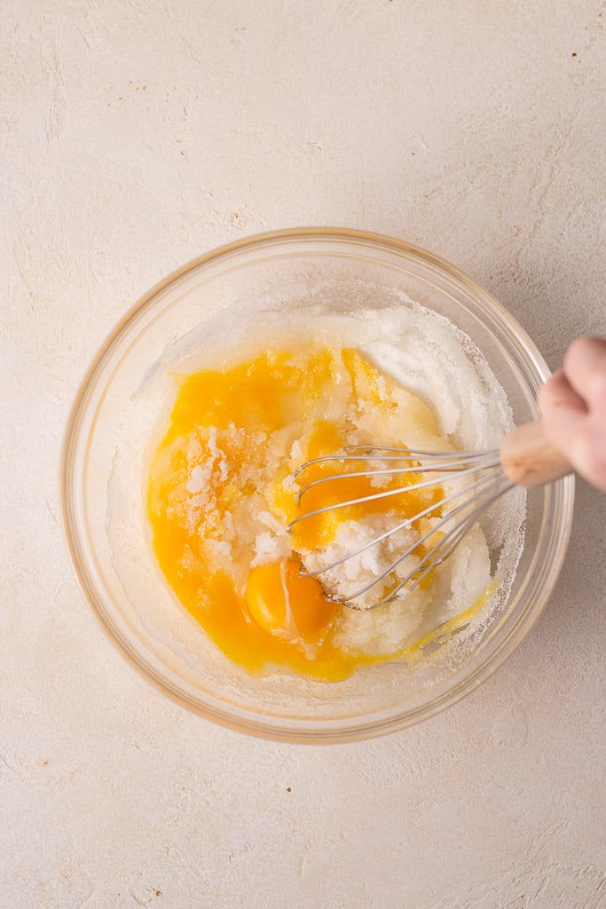 hand stirring sugar and eggs in a bowl.