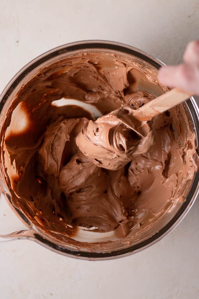 hand stirring chocolate French buttercream in a stand mixer bowl
