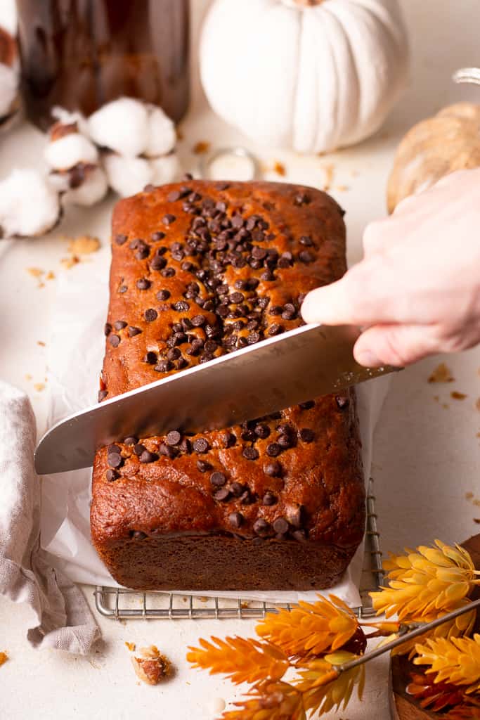 hand slicing a piece of chocolate chip pumpkin bread from the loaf