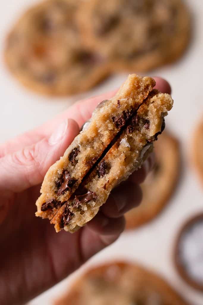 hand holding salted caramel chocolate chip cookies from the side. The cookie is split in half