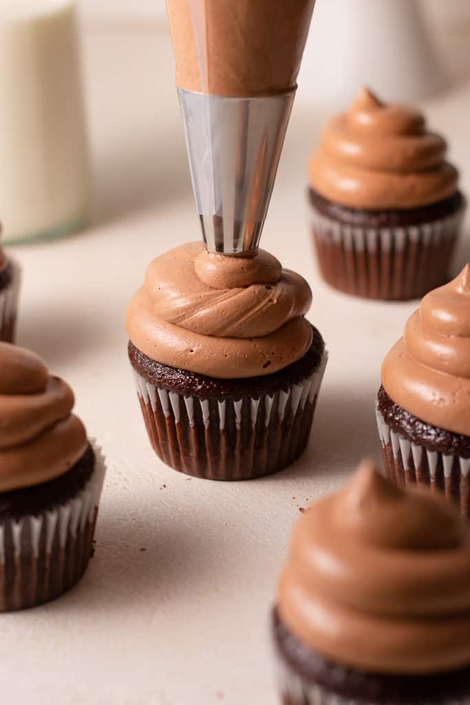 piping tip frosting buttercream onto chocolate fudge cupcakes