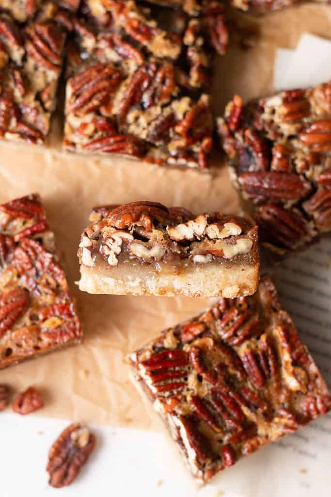 honey pecan pie bars on a piece of parchment paper and one of the bars flipped on it's side so you can see the inside.
