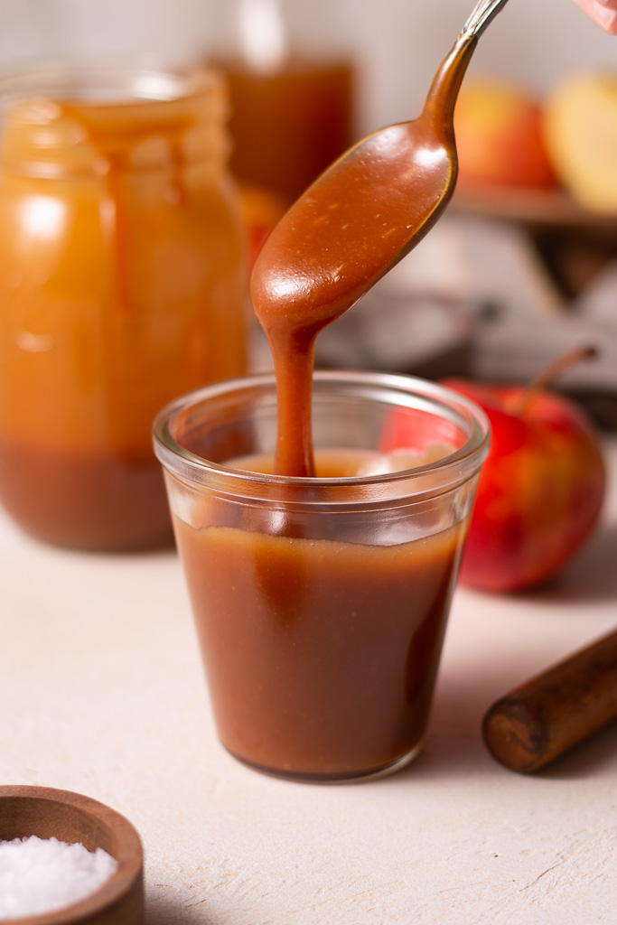 side shot of a spoon drizzling apple cider caramel sauce into a glass container