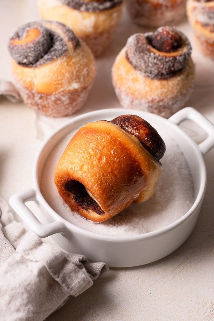 uncoated chocolate bread roll being rolled in butter and sugar.