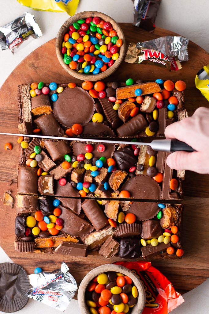 overhead shot of a hand slicing leftover halloween candy brownies down the middle.