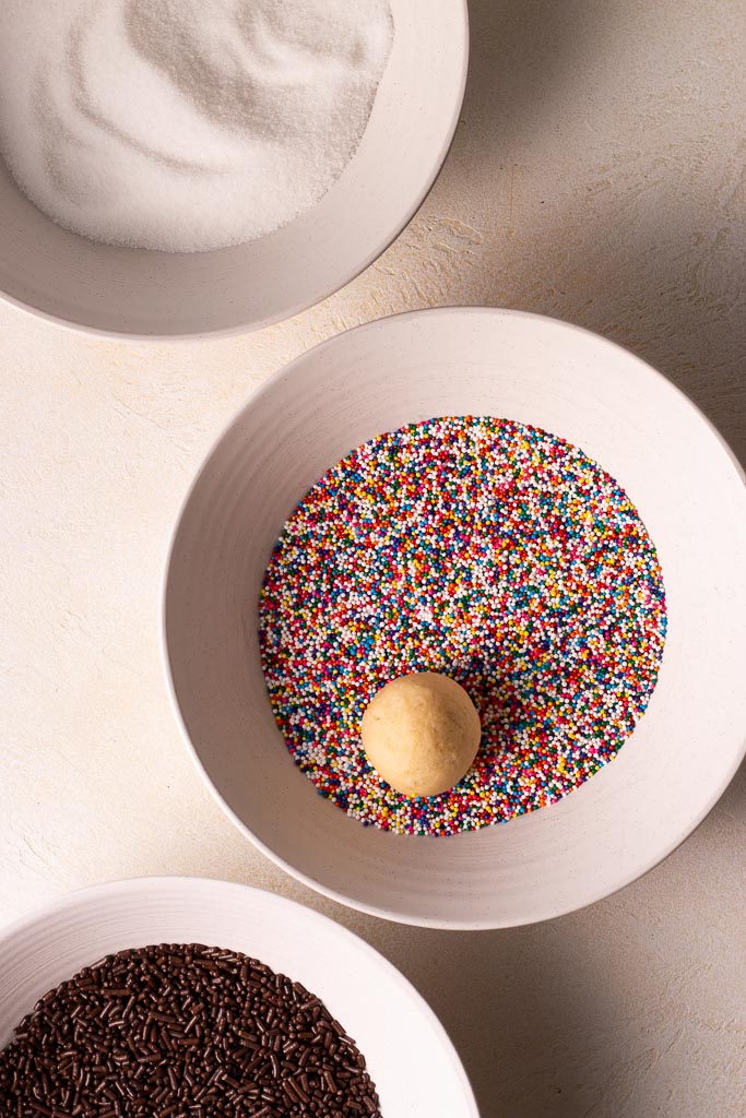 soft and chewy vanilla bean sugar cookies cookie dough ball in a bowl of sprinkles.