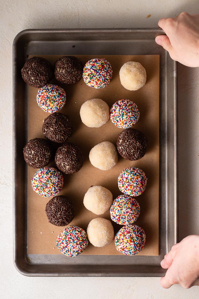 hands moving a cookie sheet to a board full of cookie dough balls.