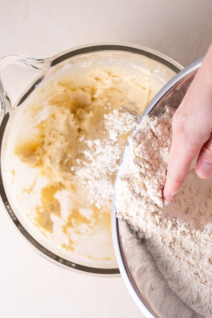 adding dry ingredients to creamed butter and sugar in a stand mixer bowl.