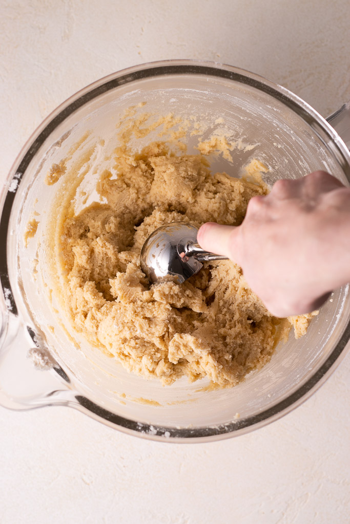 hand scooping dough from stand mixer bowl.