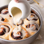 chocolate cinnamon rolls in a pan having glaze poured on top.