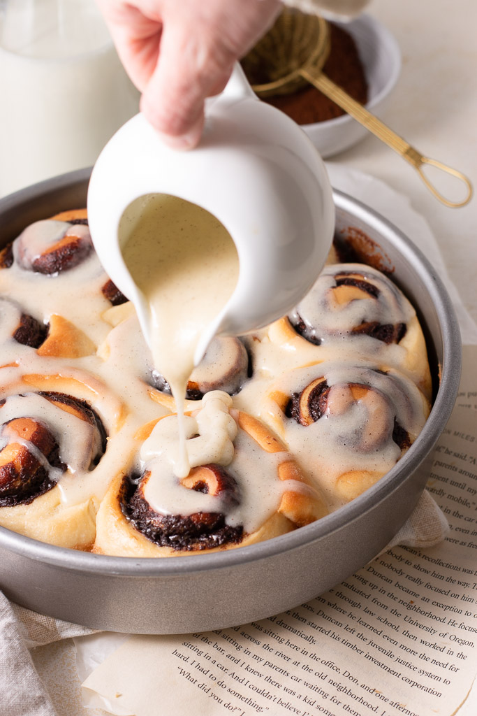 chocolate cinnamon rolls in a pan having glaze poured on top.