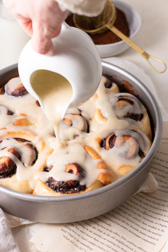 hand pouring glaze onto chocolate cinnamon rolls.