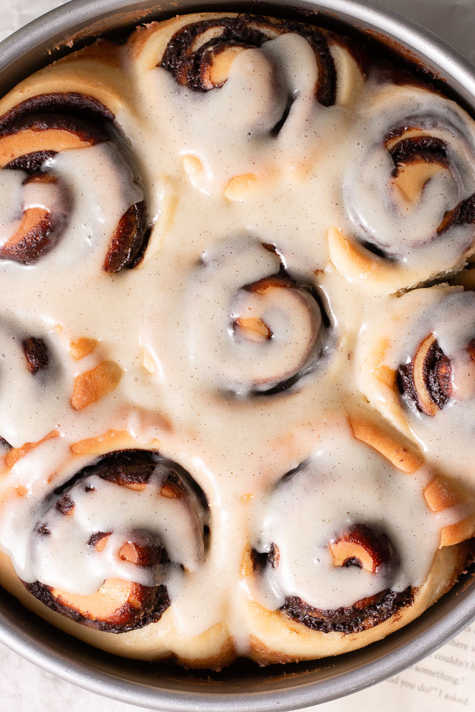 overhead shot of chocolate cinnamon rolls in a cake pan with glaze poured over it.