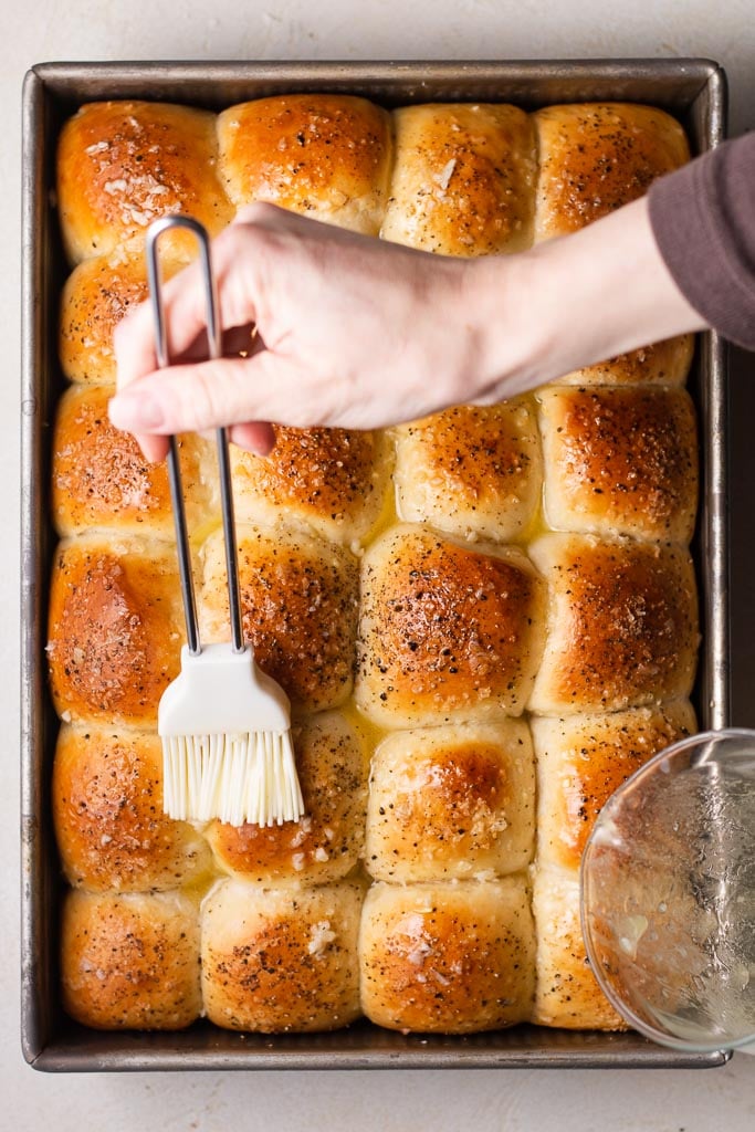 hand brushing butter onto pull apart garlic dinner rolls.