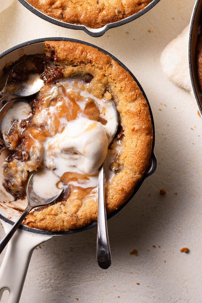 overhead shot of a mini skillet cookie recipe on a board with homemade caramel sauce and ice cream.