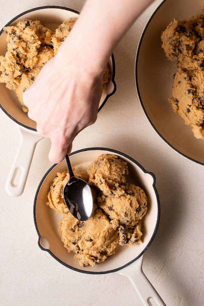 overhead shot of spooning mini skillet cookie dough into mini cast iron skillets.