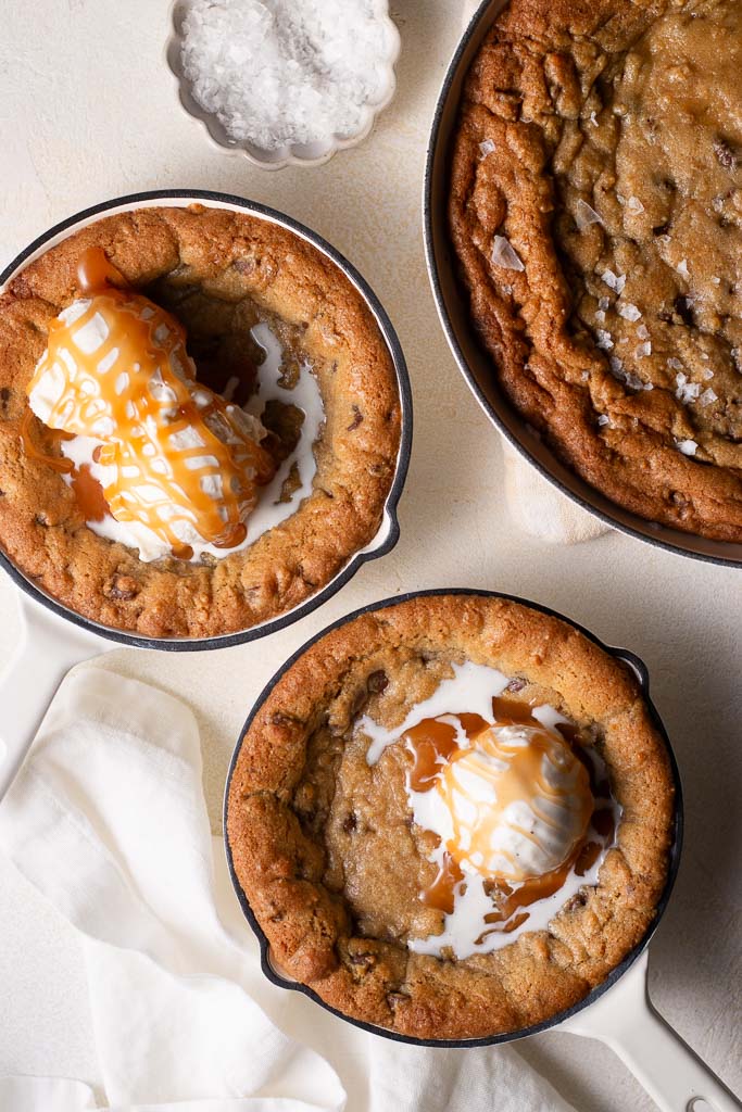 overhead shot of mini skillet cookies on a board with homemade caramel and ice cream on top.